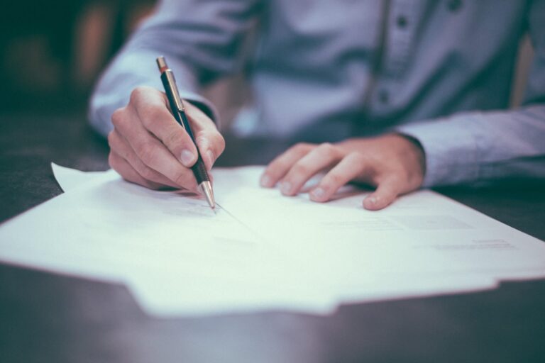 Closeup on a mans hands as he signs a piece of paper with a pen in his hand.