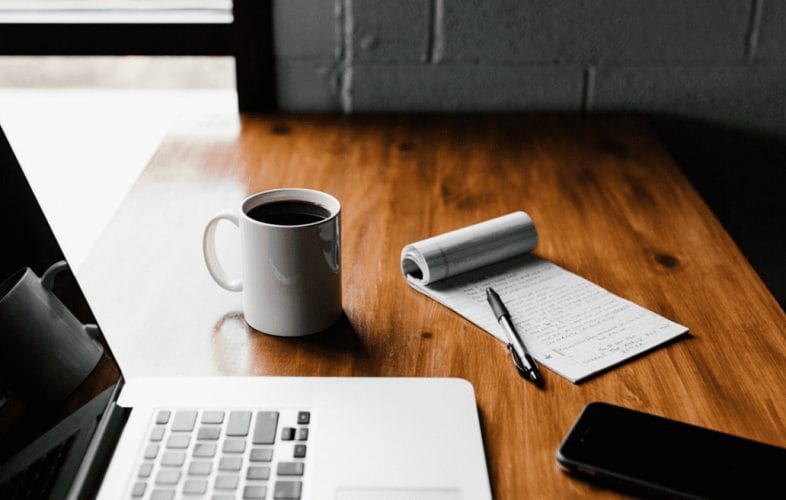 A work desk setup including a laptop, phone, pen and notepad
