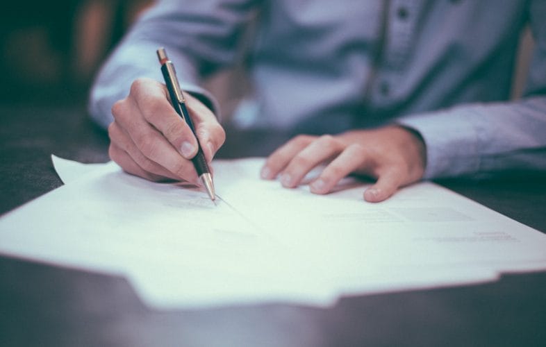 Closeup on a mans hands as he signs a piece of paper with a pen in his hand.